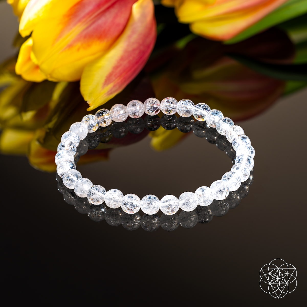 Clear beaded bracelet on a reflective surface with flowers in the background