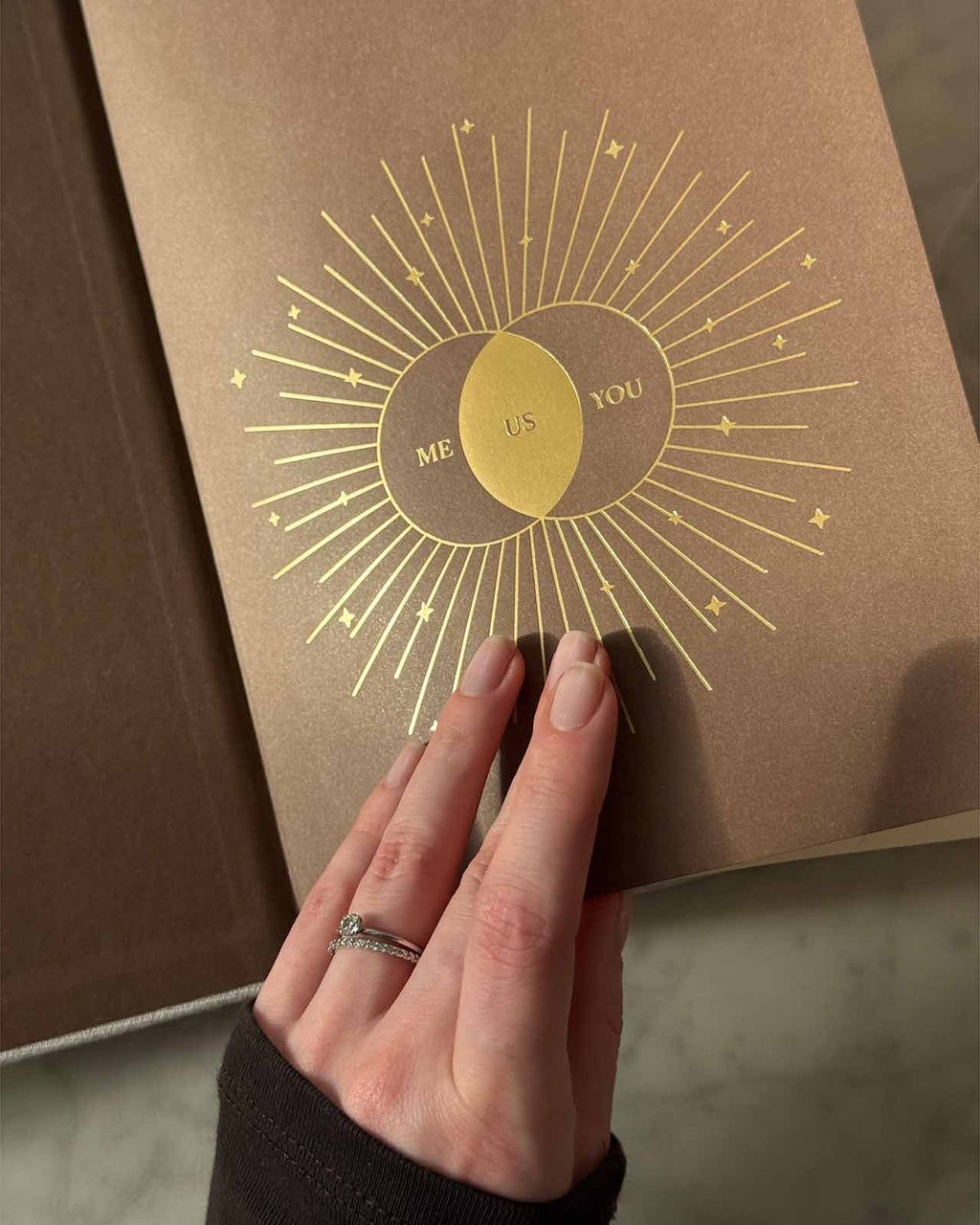 Brown book with gold 'Me Us You' design held by a hand