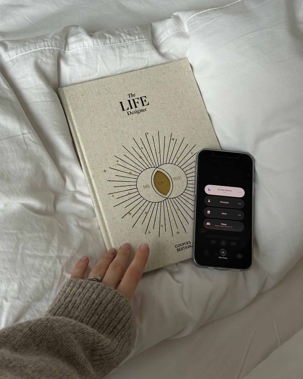 Book titled 'The Life Designer' on a white surface with a hand and phone beside it.