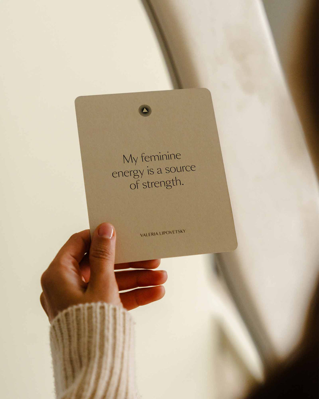 Hand holding a card with a quote about feminine energy and strength, blurred background