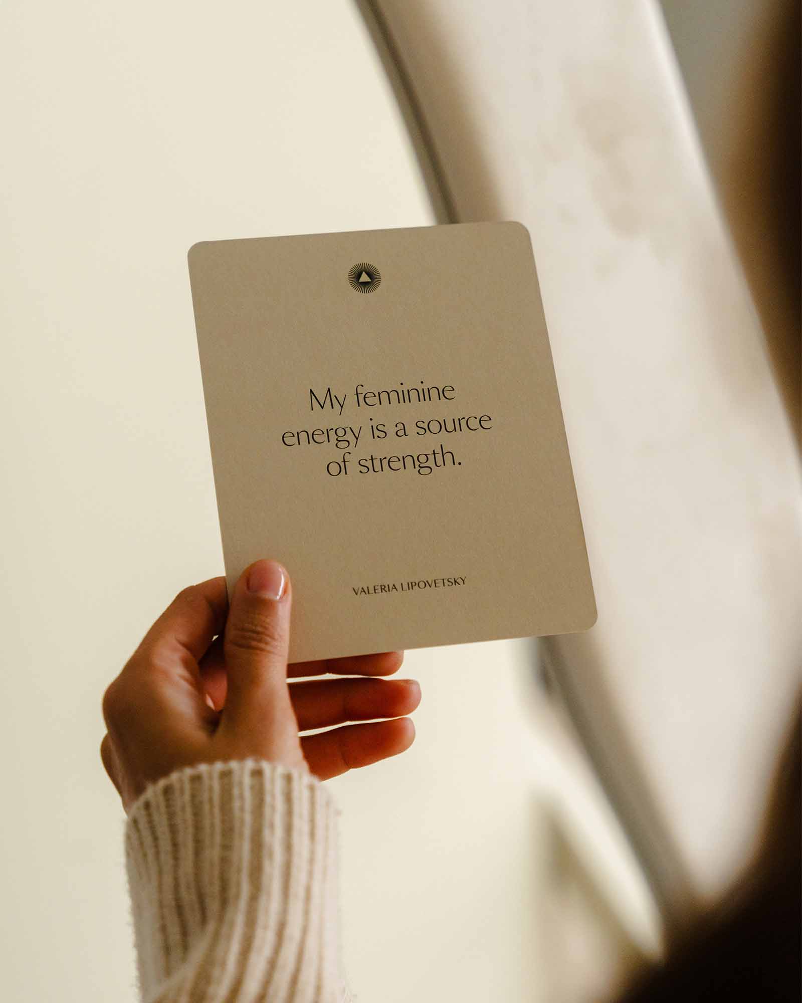 Hand holding a card with a quote about feminine energy and strength, blurred background