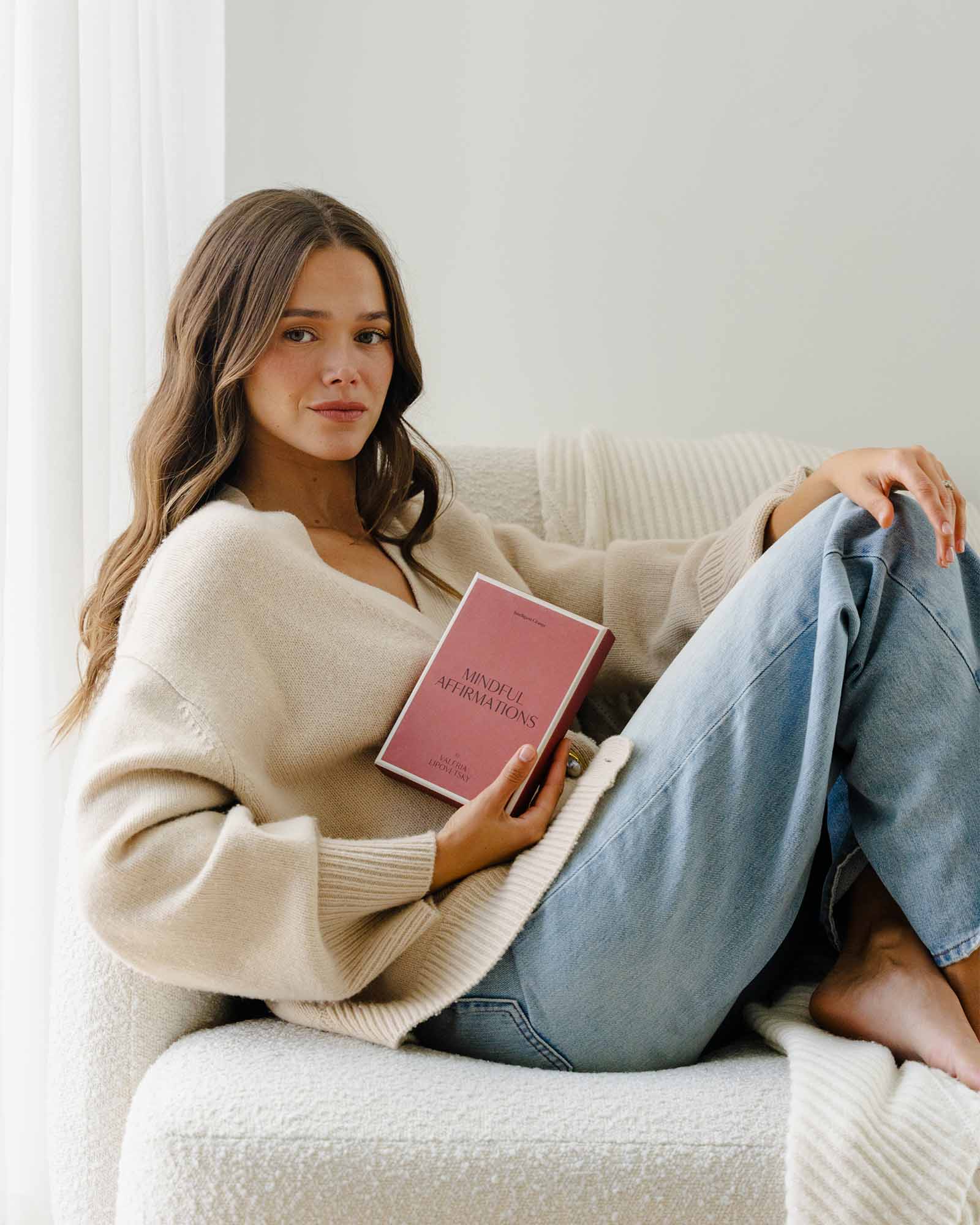 Woman sitting on a couch holding a pink book with a white background