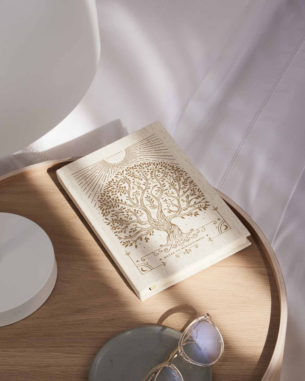 Open book with tree design on a wooden surface with sunglasses and a white plate.