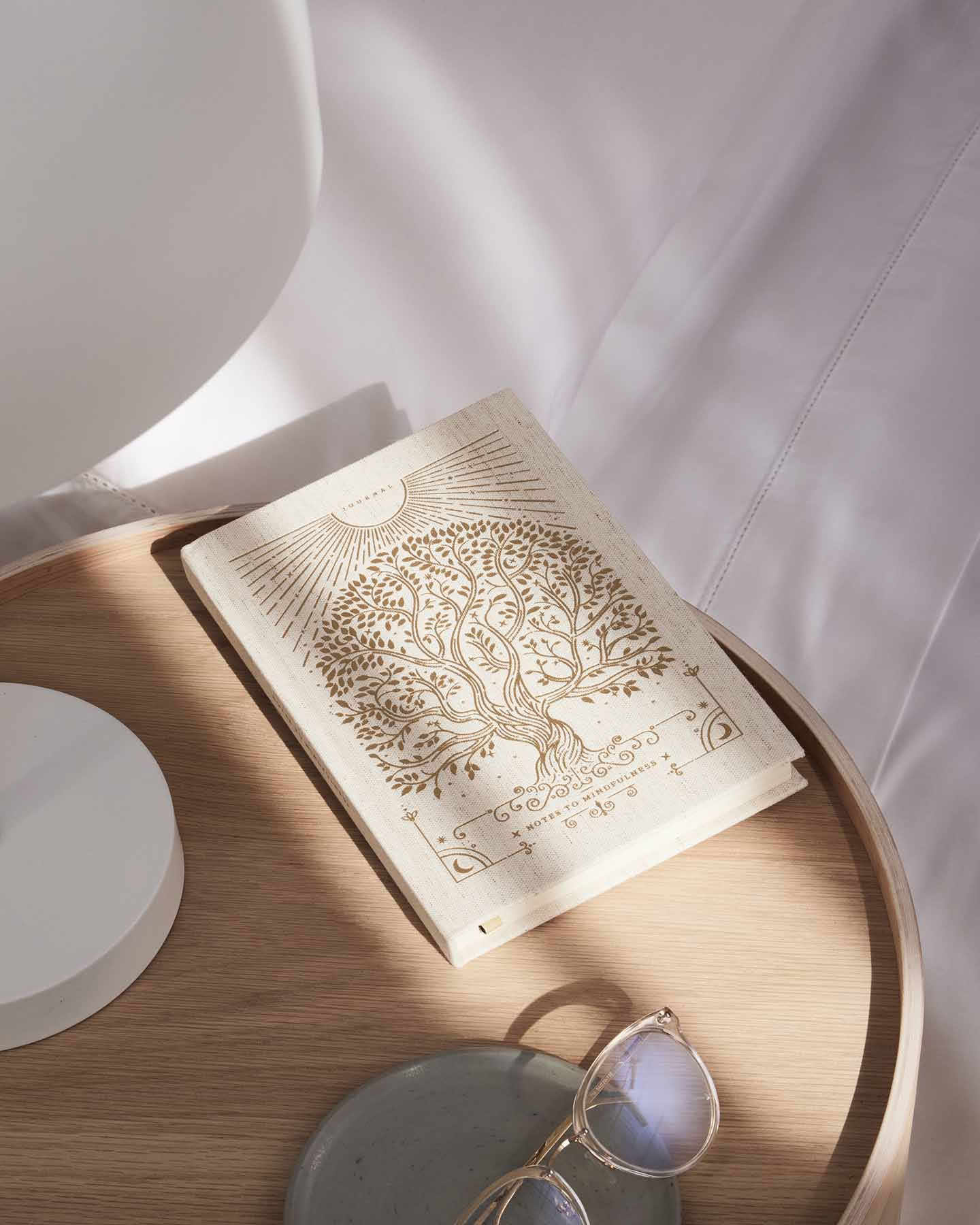 Open book with tree design on a wooden surface with sunglasses and a white plate.