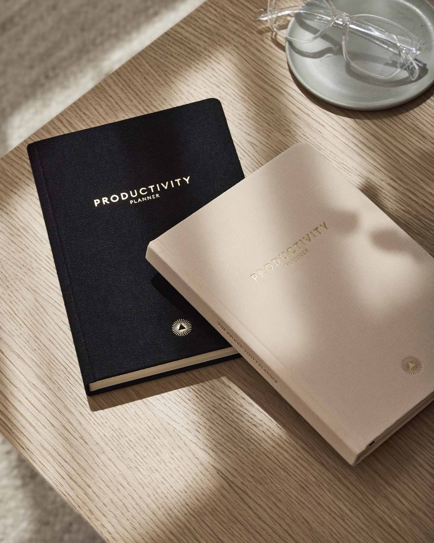 Two 'Productivity Planner' notebooks, one black and one beige, on a wooden surface.