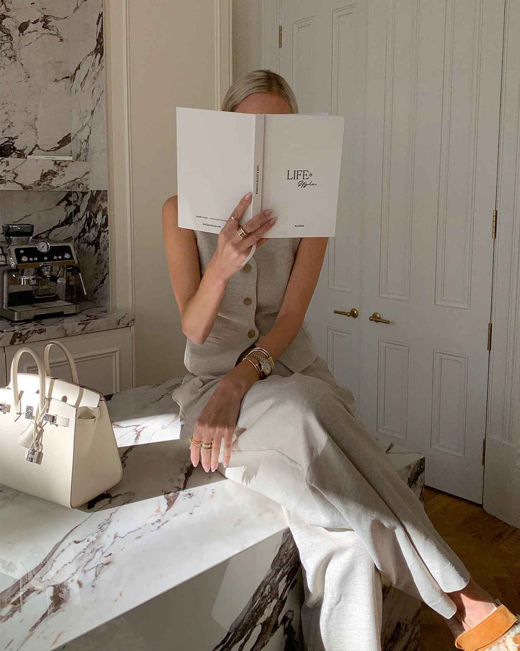 Person sitting on a marble bench holding a book titled 'LIFE' in a stylish room.