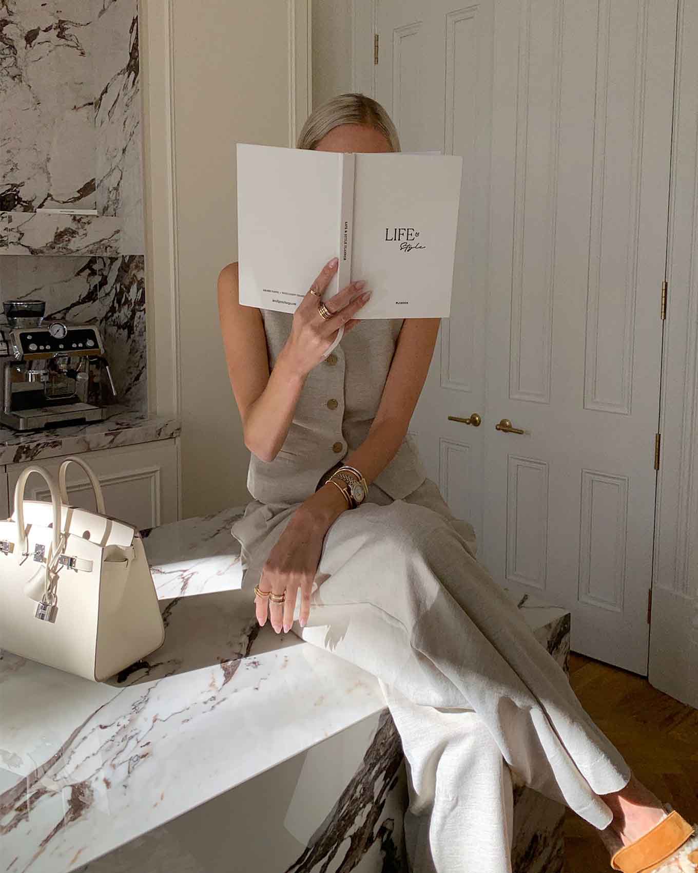 Person sitting on a marble bench holding a book titled 'LIFE' in a stylish room.