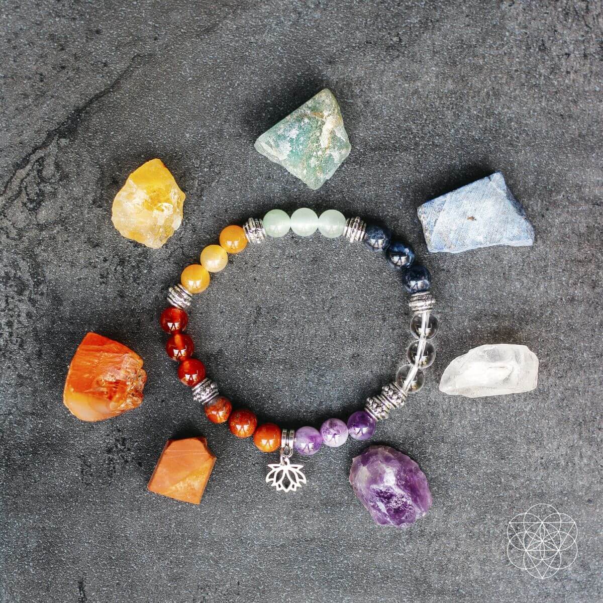 Colorful beaded bracelet with tree of life charm on a dark surface with crystals around it