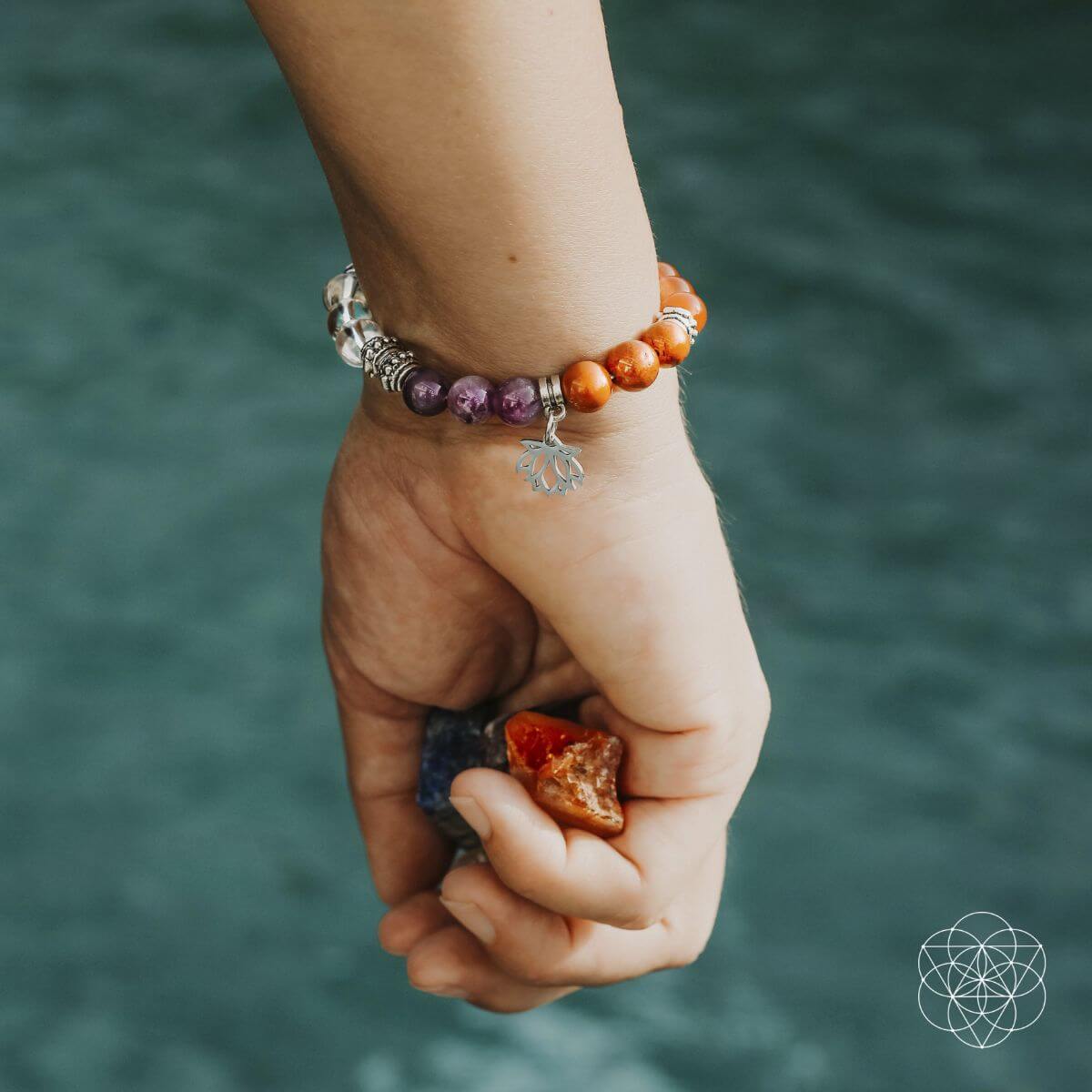 Hand wearing a bracelet with beads and charms against a blurred natural background