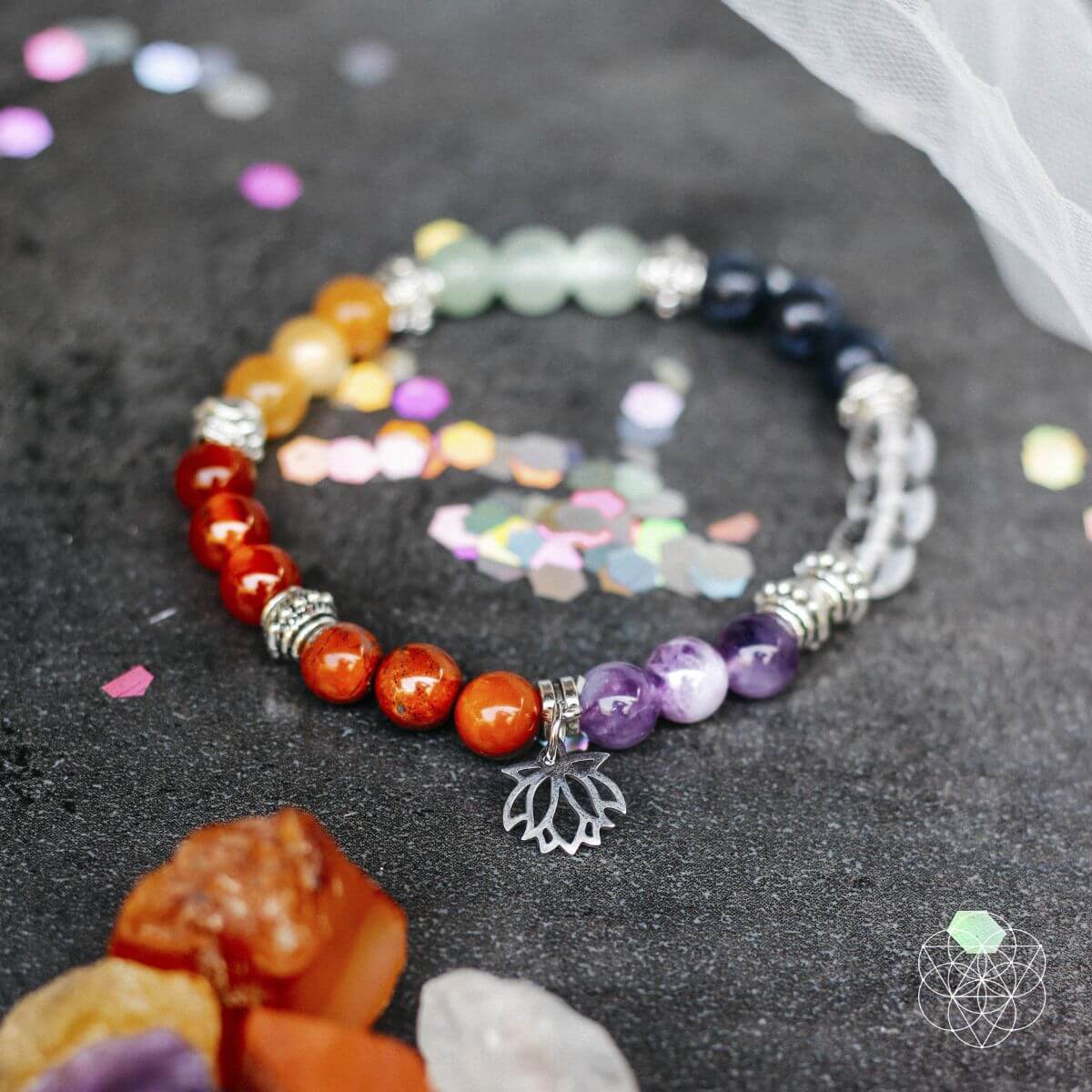 Multicolored beaded bracelet with a silver leaf charm on a dark surface with crystals and confetti.