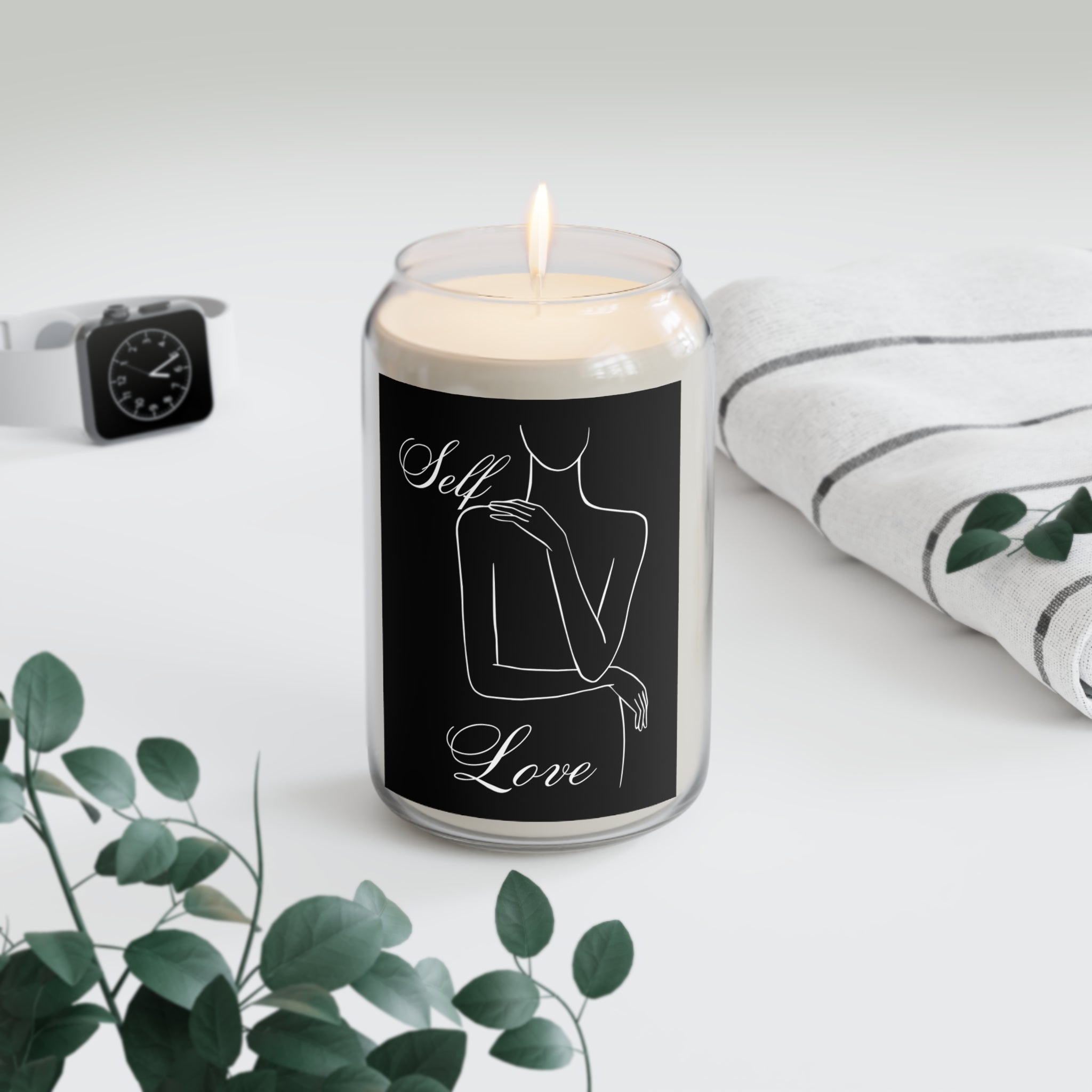 Candle with 'Self Love' label on a white surface with greenery