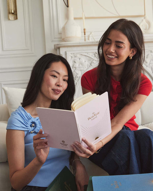 Two women sitting together, looking at a product in a luxurious room.
