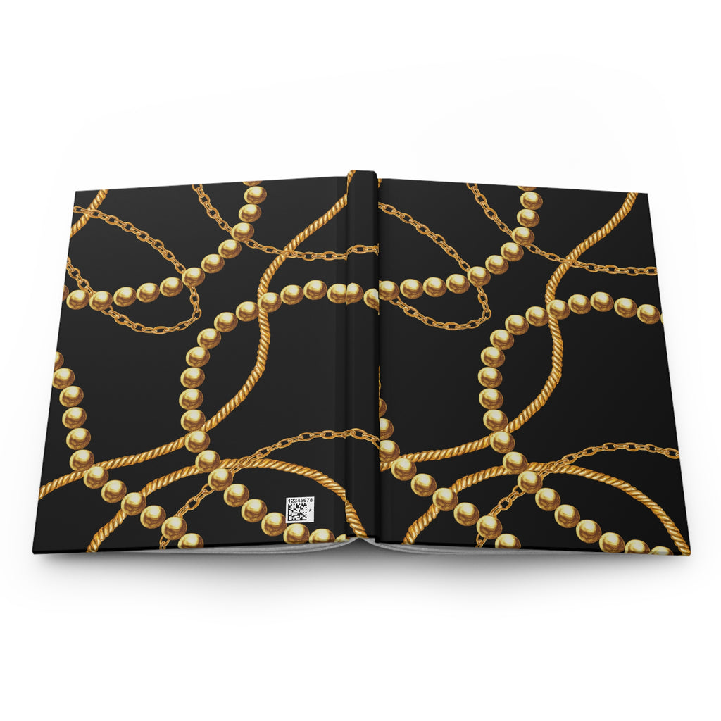 An open hardcover book or notebook displayed flat against a white background, featuring a black cover design with an elegant repeating pattern of gold chains and pearl-like beads.