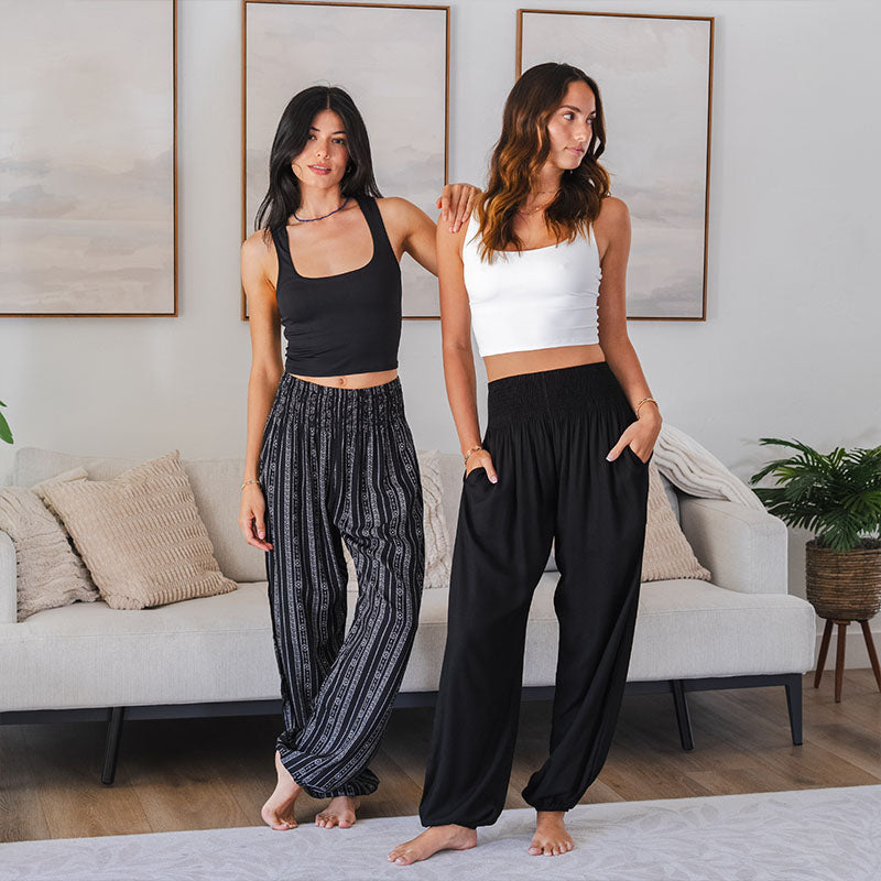 Two women standing in a living room wearing casual outfits with wide-leg pants.