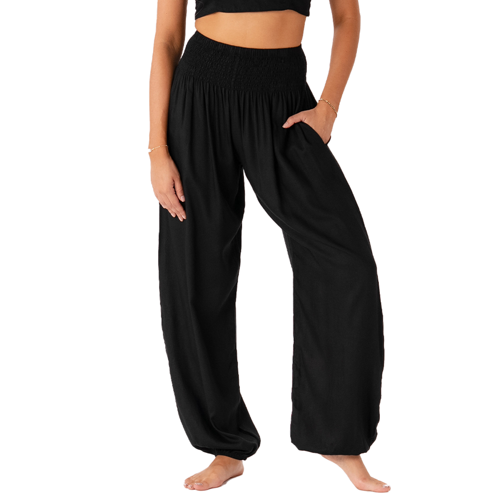 A model wearing black harem-style pants with a smocked elastic waistband, side pockets, and a loose, flowing silhouette, shown against a plain white background.