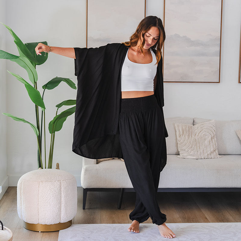 Woman in a black outfit standing in a living room with a plant and sofa in the background