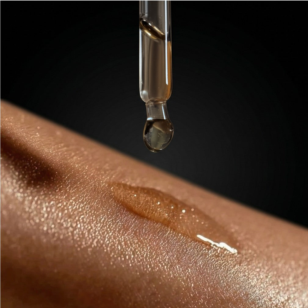 Dropper with a drop of oil being applied to skin on a dark background