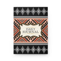 A hardcover daily journal with a geometric Southwestern-style pattern. The cover features black borders at the top and bottom with white diamond motifs, a central cream-colored label reading 'DAILY JOURNAL', and a middle band with orange, black, and beige geometric patterns.
