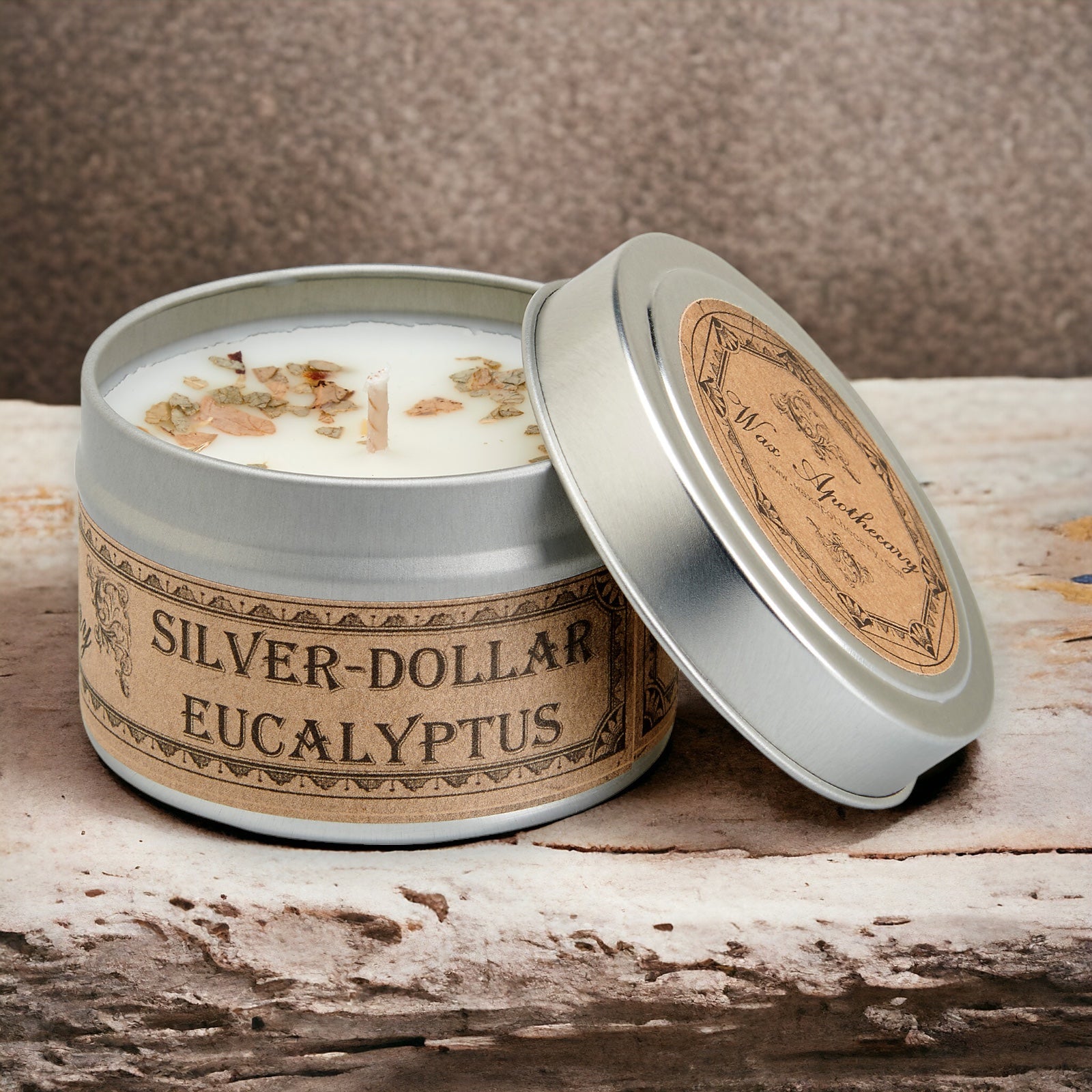 Candle in a tin labeled 'Silver-Dollar Eucalyptus' on a wooden surface.