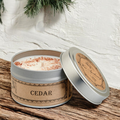 Cedar-scented candle in a tin with a wooden lid on a textured surface.