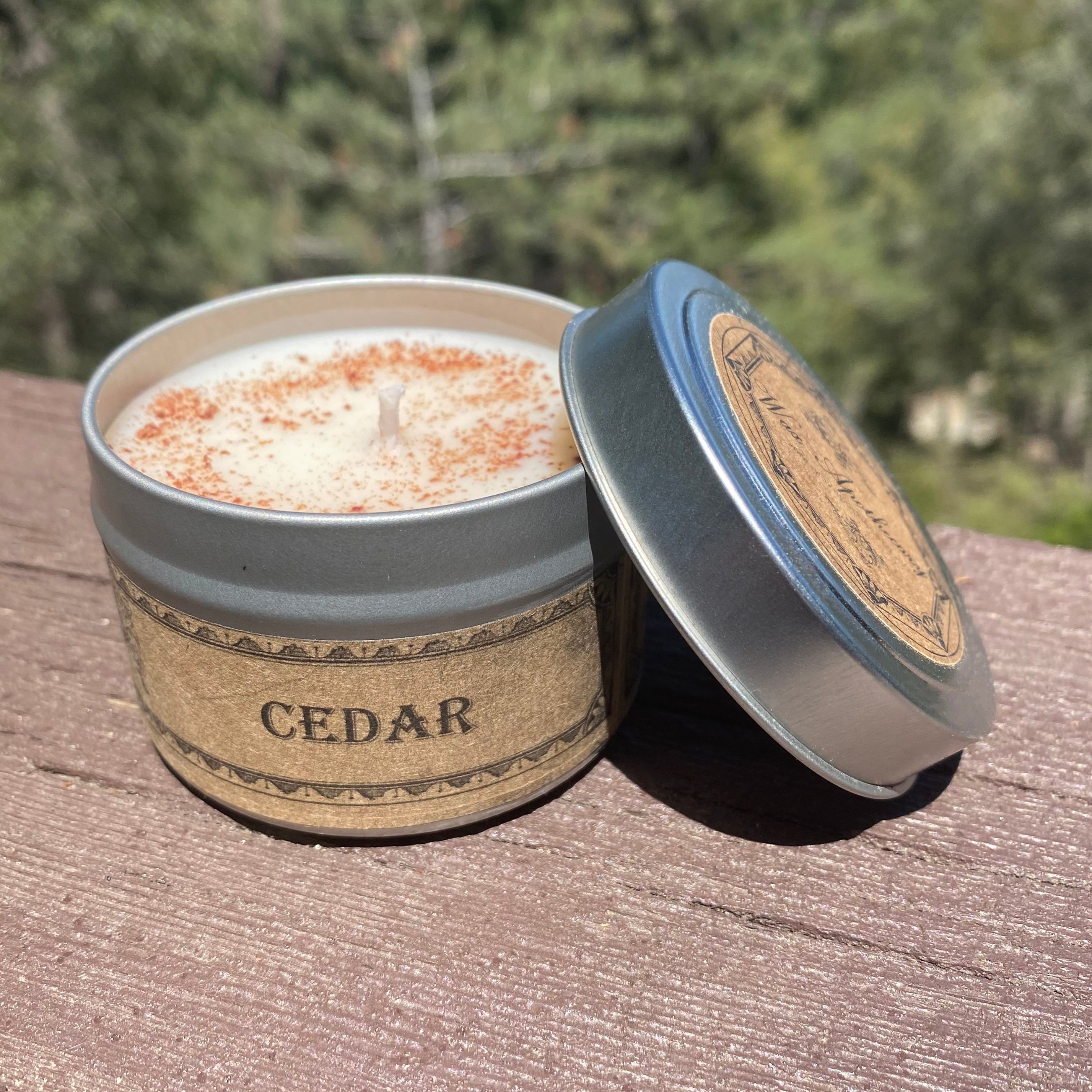 Cedar-scented candle in a tin with a wooden lid on a wooden surface with a blurred natural background.
