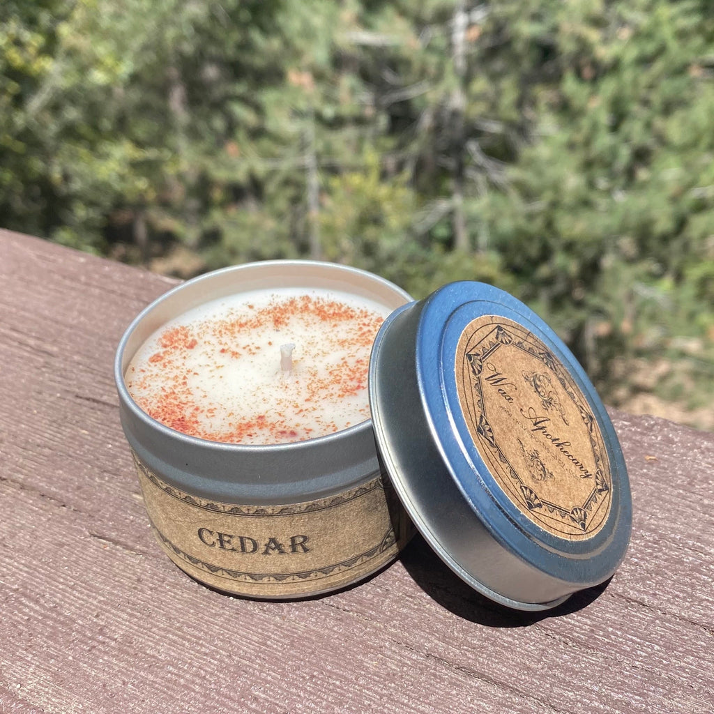 Cedar-scented candle in a tin with a wooden lid on a wooden surface with a forest background.