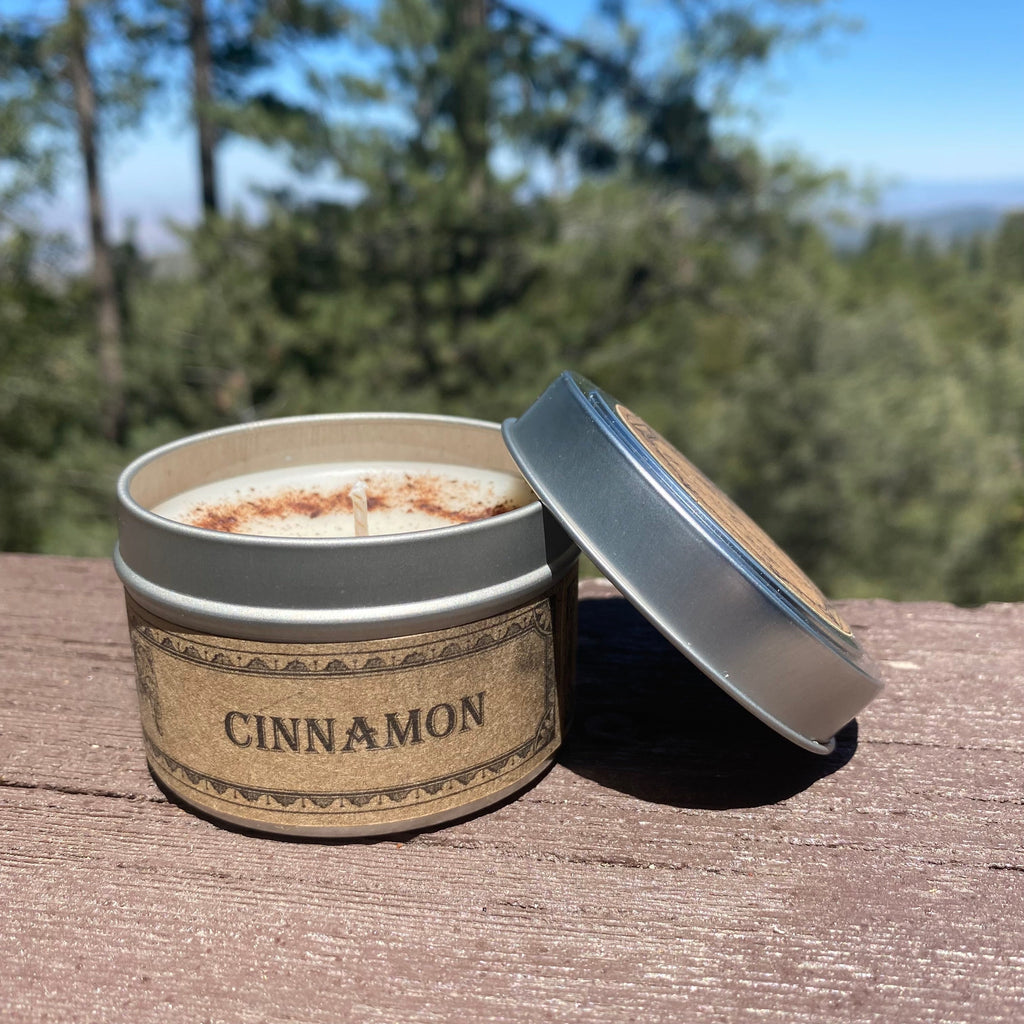 Cinnamon-scented candle in a tin with a lid on a wooden surface outdoors.