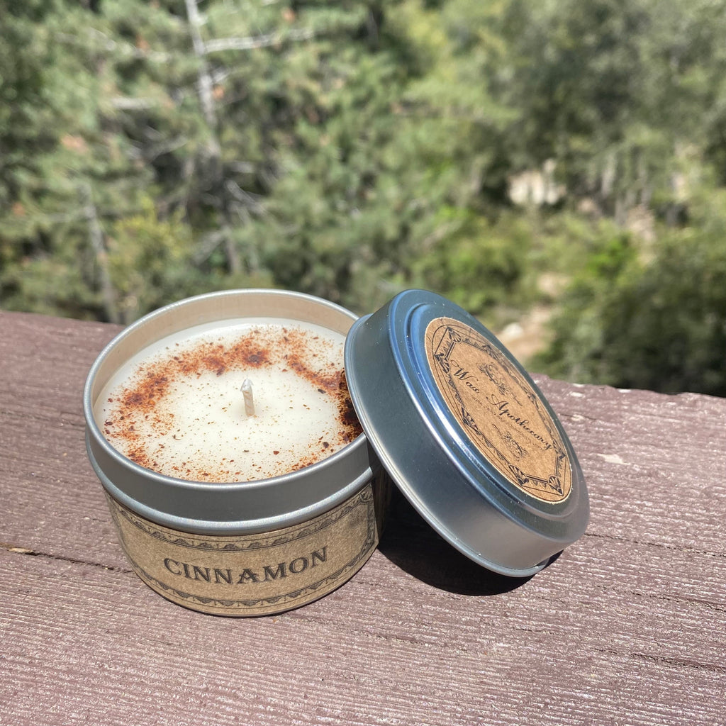 Cinnamon-scented candle in a tin with a lid on a wooden surface, outdoors.