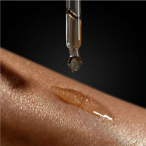 Dropper with a drop of oil being applied to skin on a dark background