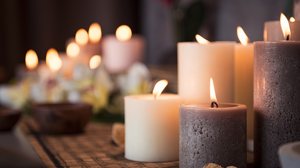 Candles of various sizes and colors on a textured surface with a blurred background