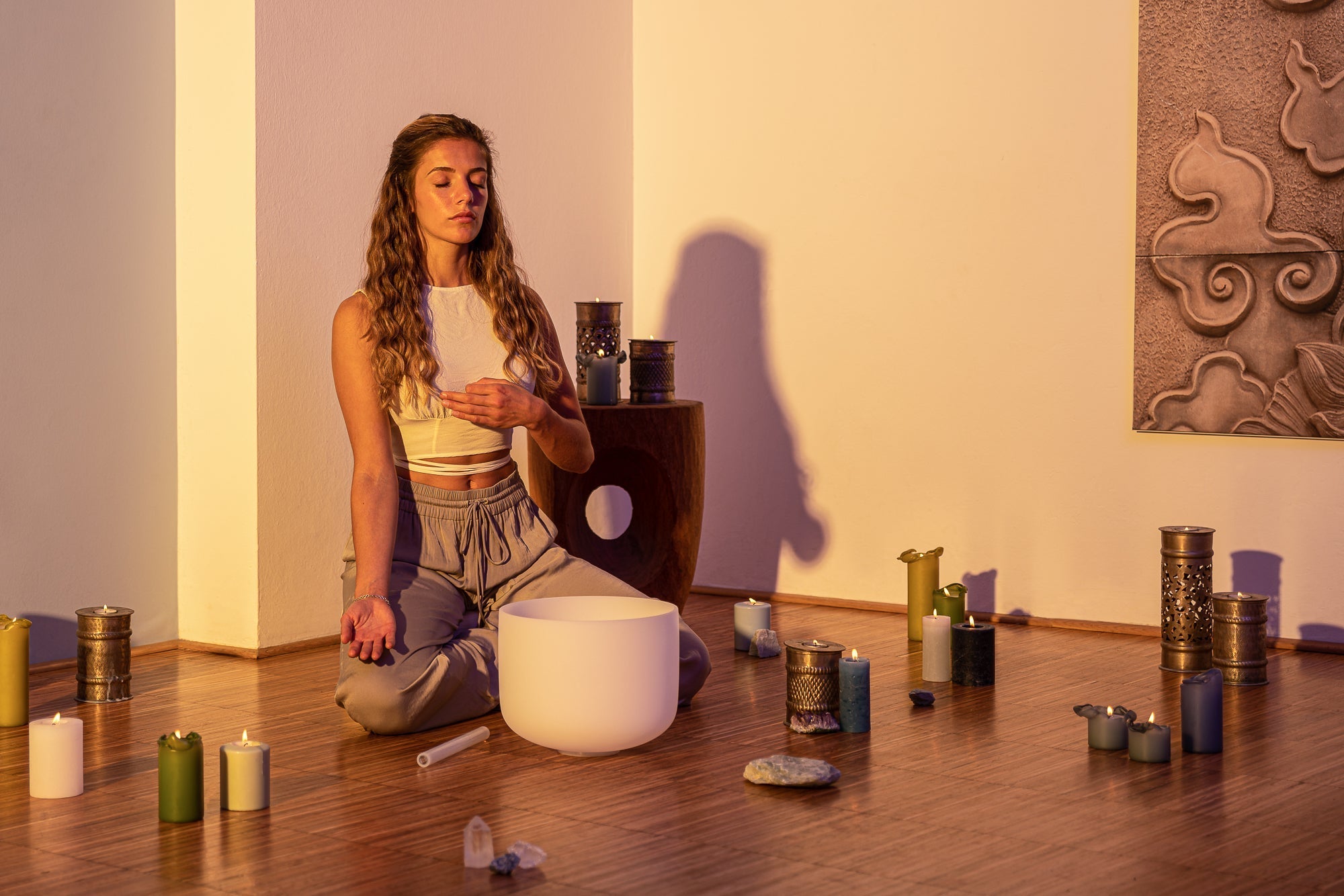Woman sitting in a meditative pose with a white bowl in a room with candles and incense.