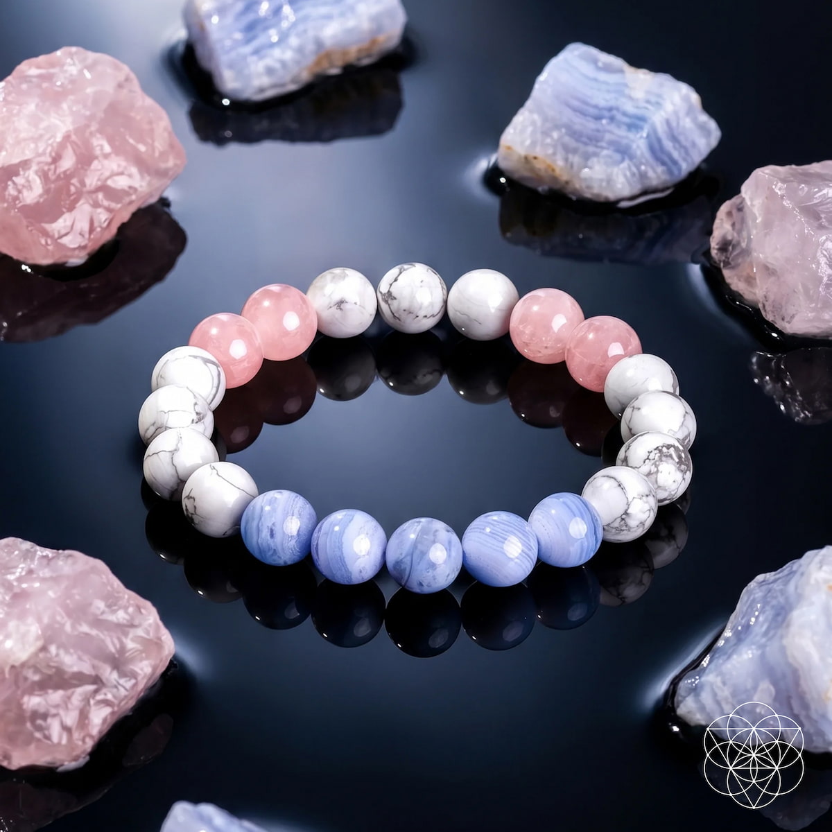 A beaded stretch bracelet made of alternating light pink, lavender-blue, and white/gray marbled beads, displayed on a glossy black reflective surface surrounded by pink and blue crystals.