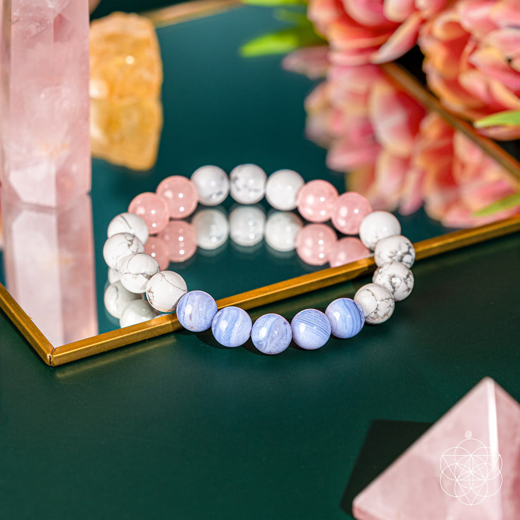 Multicolored beaded bracelet on a reflective surface with flowers and crystals in the background