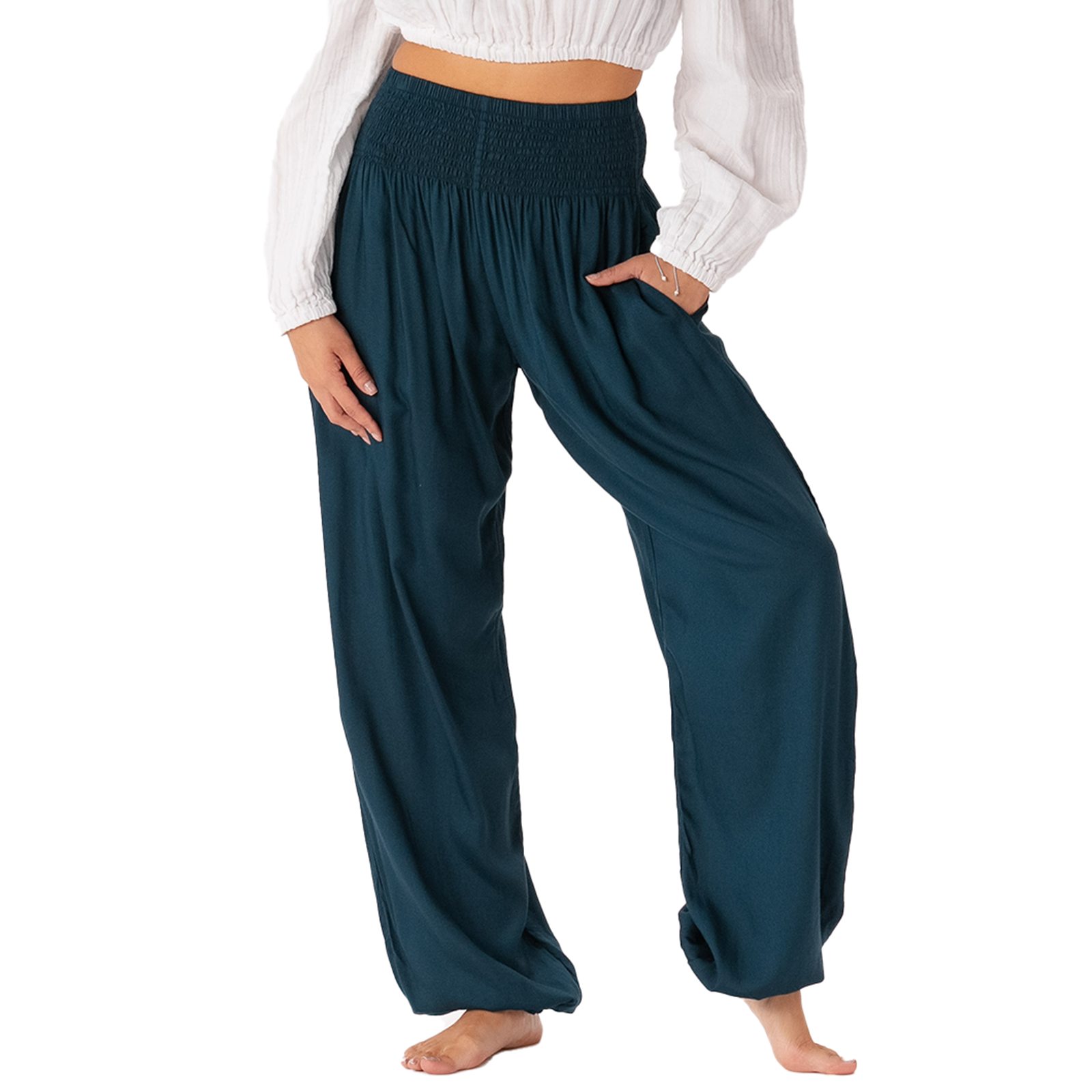 A person modeling loose, wide-leg harem-style pants in a deep teal-blue color, paired with a white long-sleeve crop top. The pants feature a gathered elastic waist, side pockets, and a relaxed drape, shown against a plain white background.