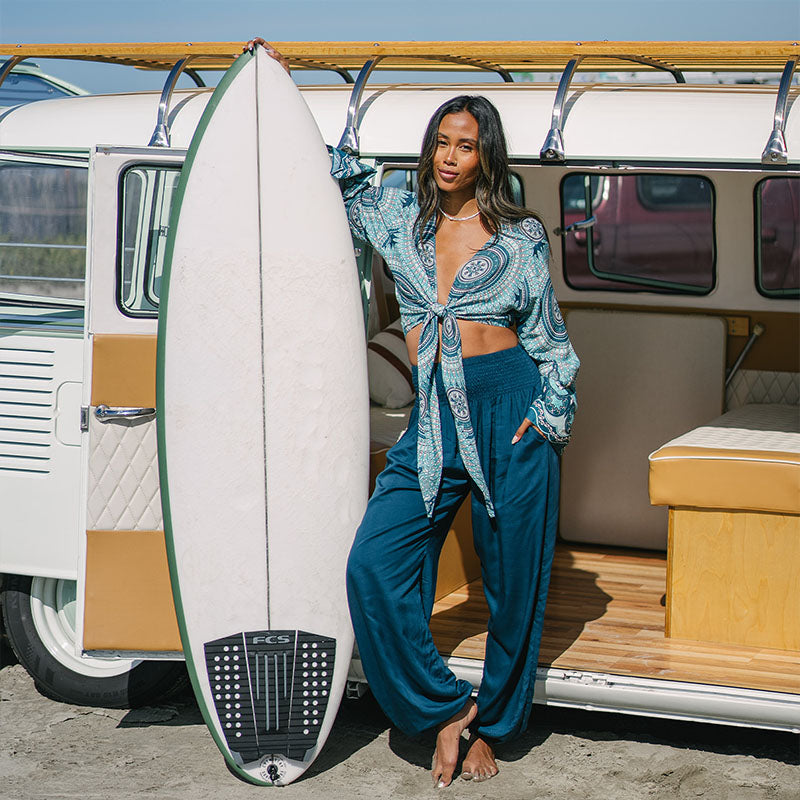 Woman in a blue outfit holding a surfboard next to a vintage van.
