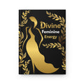 A black hardcover journal or notebook featuring a gold metallic high-heeled shoe silhouette, gold laurel leaves, and the text 'Divine Feminine Energy' on the front cover, shown against a plain white background.