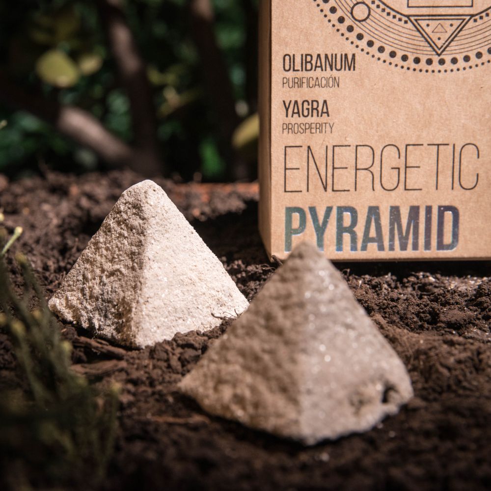 Two pyramid-shaped incense cones on soil with a cardboard box labeled 'Energetic Pyramid' in the background.