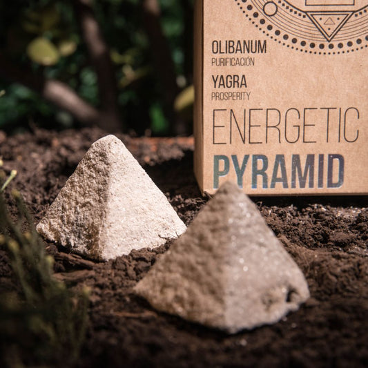 Two pyramid-shaped incense cones on soil with a cardboard box labeled 'Energetic Pyramid' in the background.
