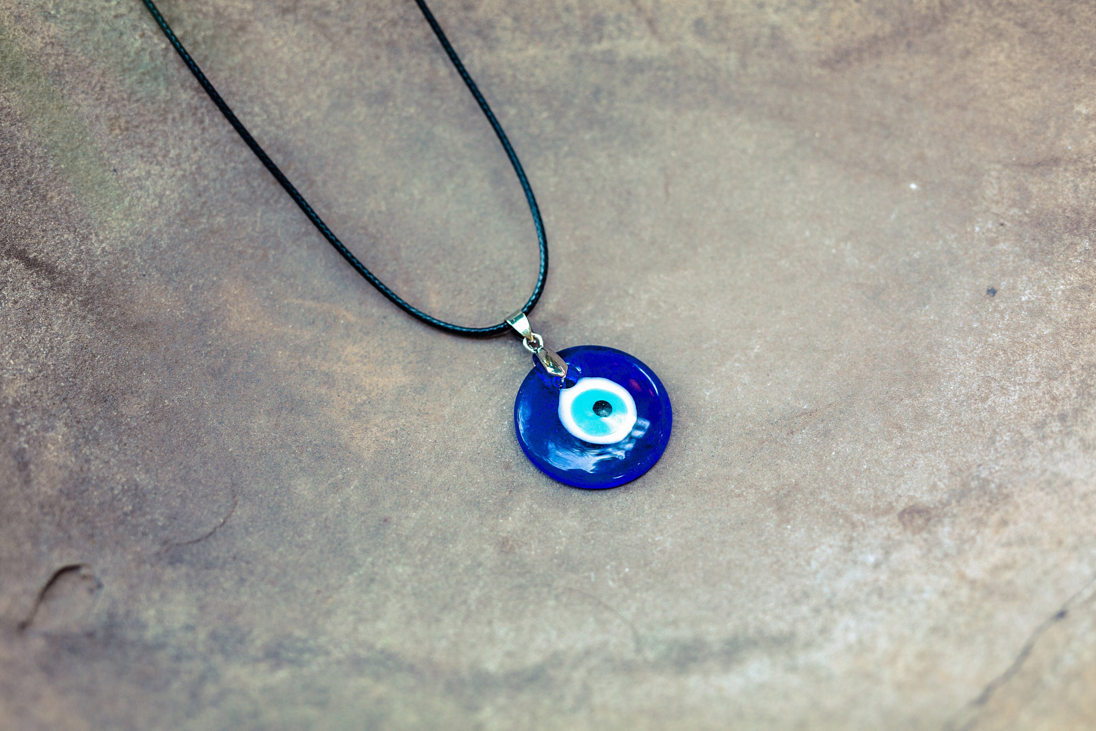 Blue evil eye pendant necklace on a textured surface