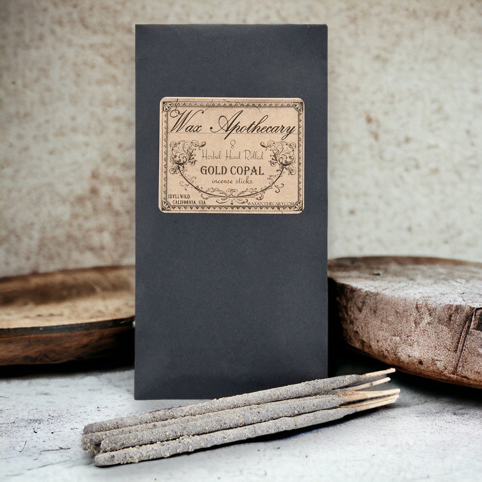 Black box with 'Wax Apothecary' label and incense sticks on a textured surface