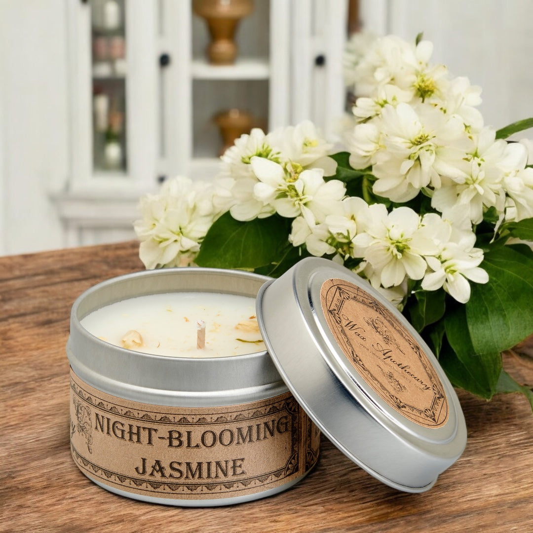 Candle in a tin labeled 'Night-Blooming Jasmine' with flowers on a wooden surface