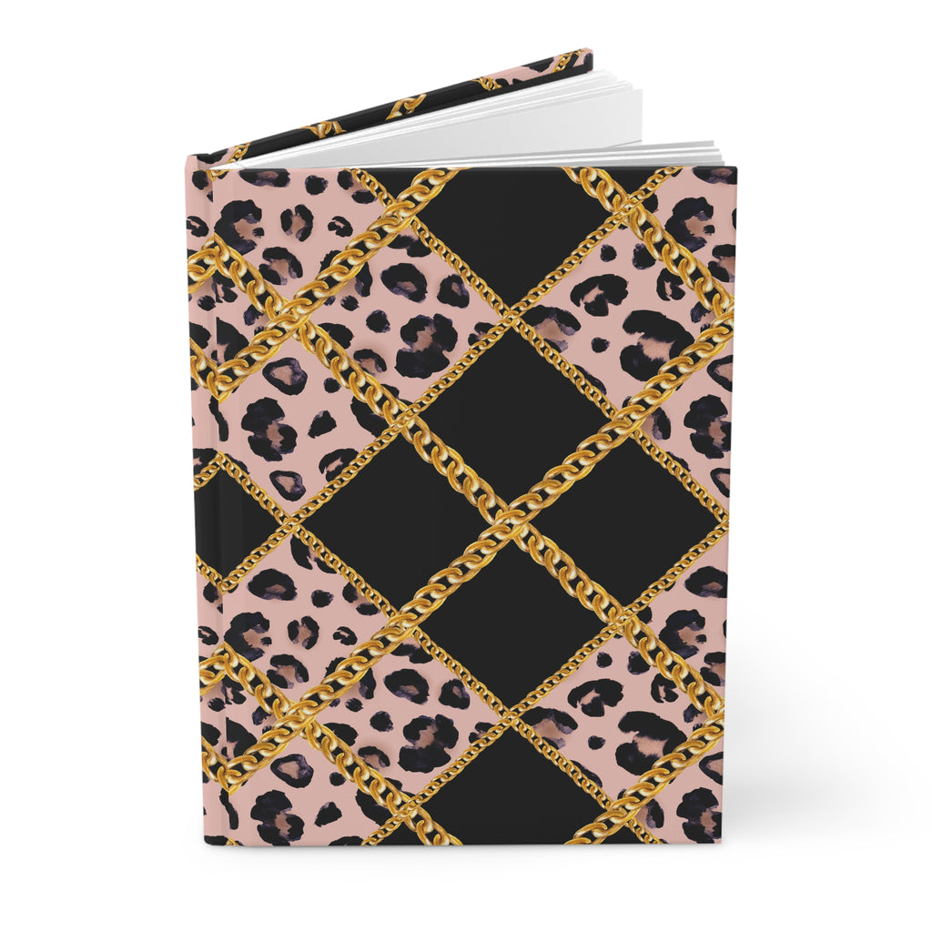 A hardcover notebook with a patterned cover featuring black leopard print, solid black diamond sections, and a gold chain-link lattice design over a dusty pink background, shown on a clean white background.