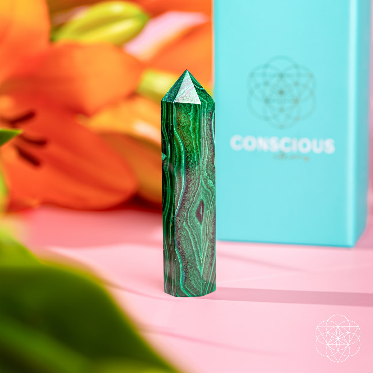 Green crystal with 'Conscious' box and orange flowers in the background