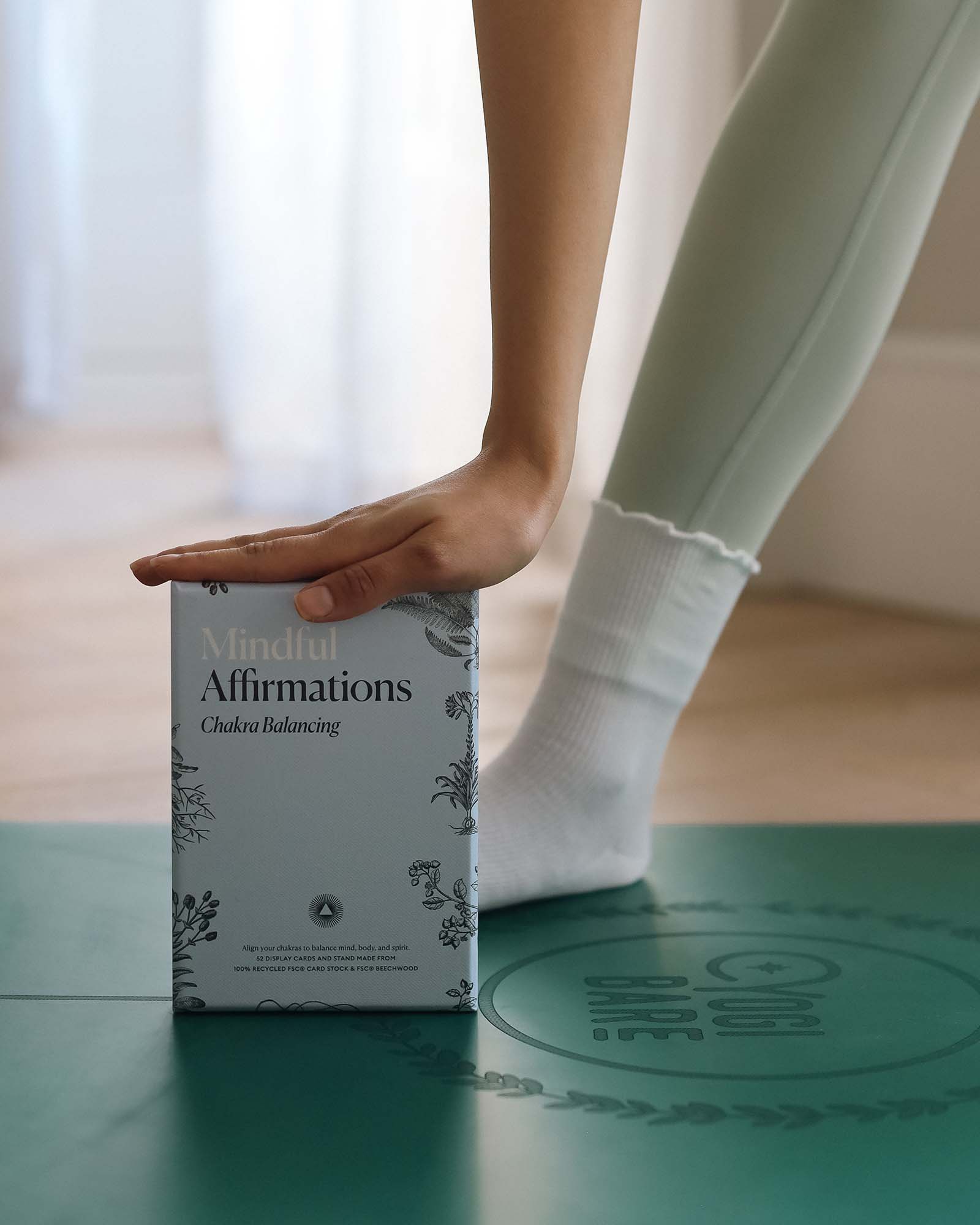 Hand reaching for a 'Mindful Affirmations' box on a green surface with a blurred background