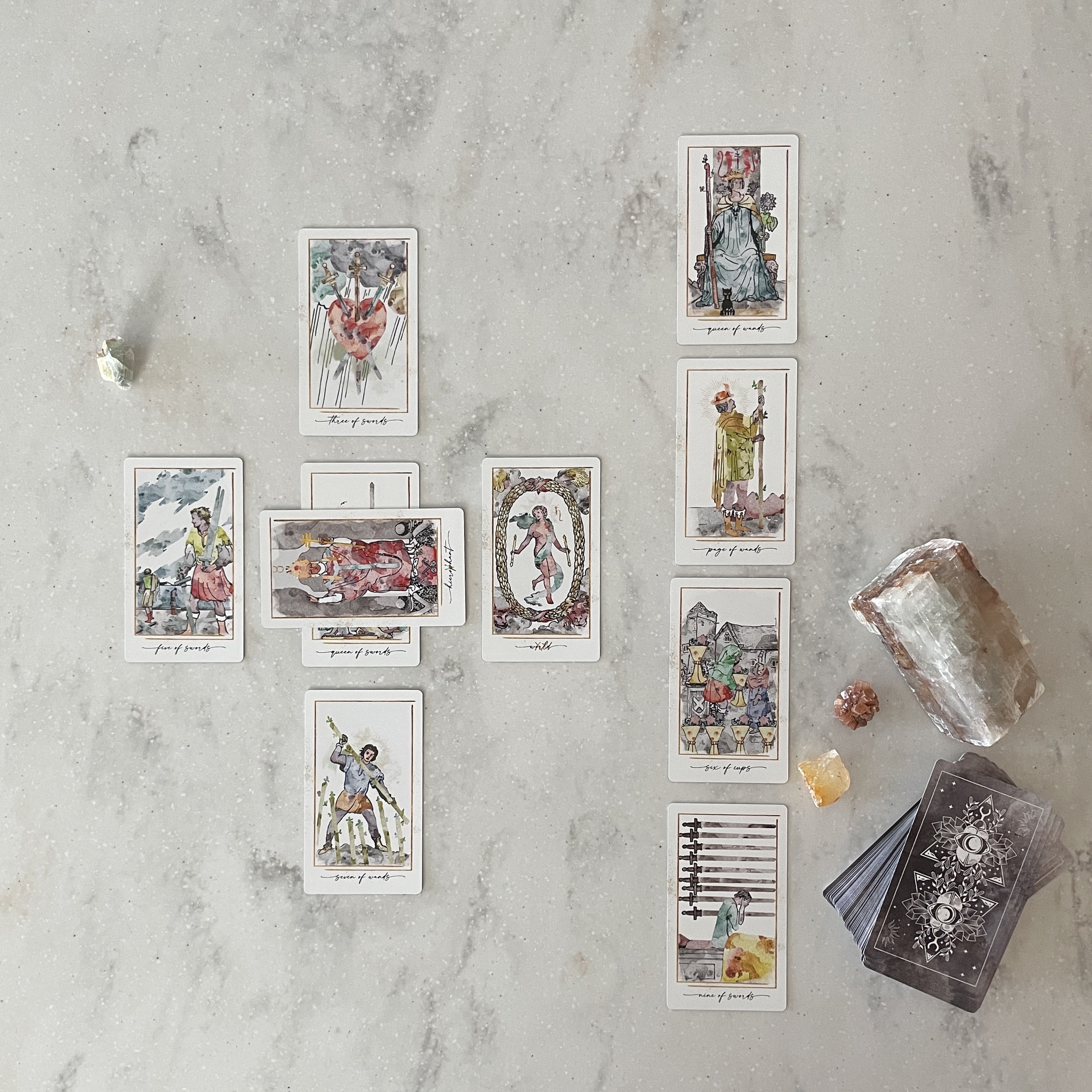 Collection of tarot cards on a textured surface with crystals and a candle.
