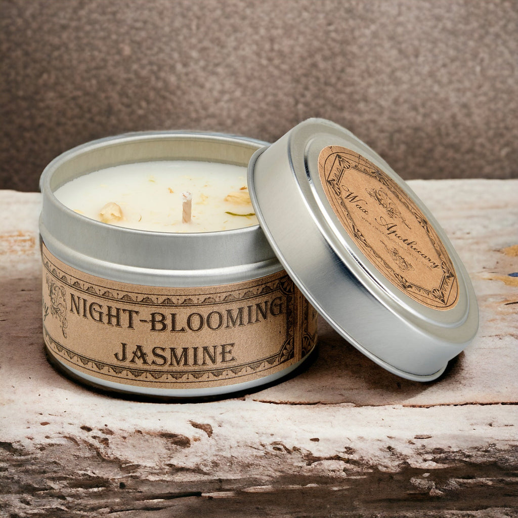Candle in a tin labeled 'Night-Blooming Jasmine' on a wooden surface.