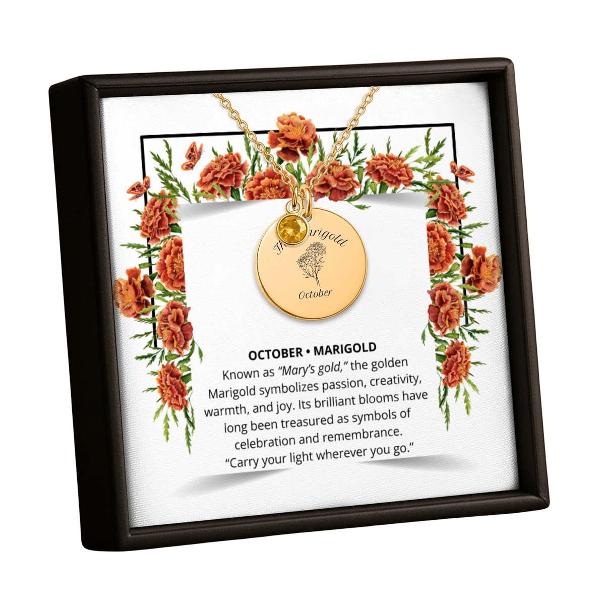 A framed monthly and yearly Marigold pendant necklace display. The black frame contains a white insert card with an illustration of orange marigold flowers, a gold necklace with a round engraved disc, and a text card titled 'OCTOBER - MARIGOLD' with a quote.