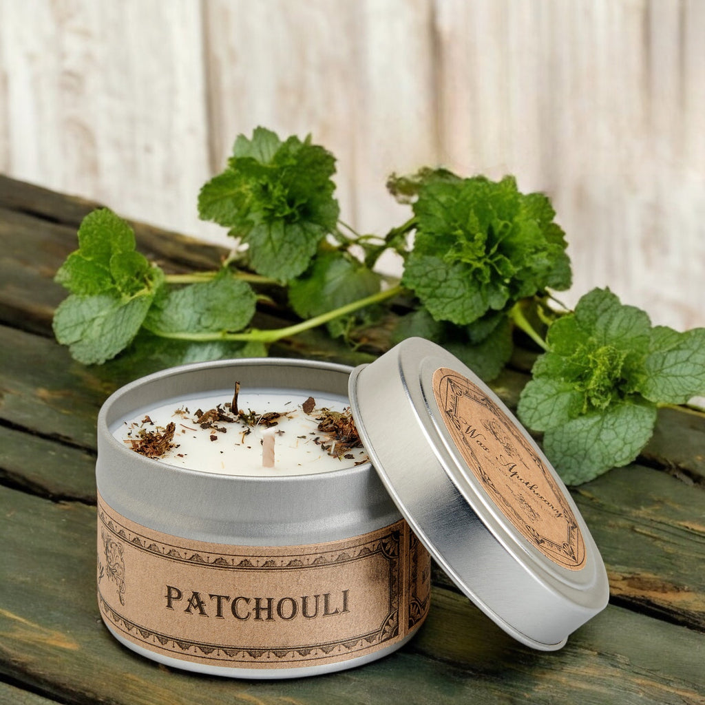 Patchouli candle in a tin with green leaves on a wooden surface