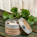 Patchouli candle in a tin with green leaves on a wooden surface