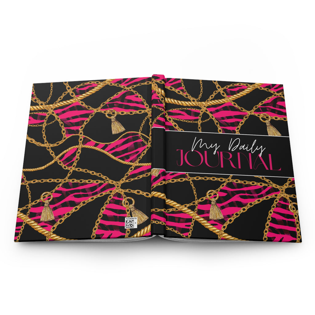 An open hardcover daily journal with a black cover decorated with a pink zebra print, gold chain patterns, and tassel charms, featuring a black title band on the spine that reads 'My Daily JOURNAL'.